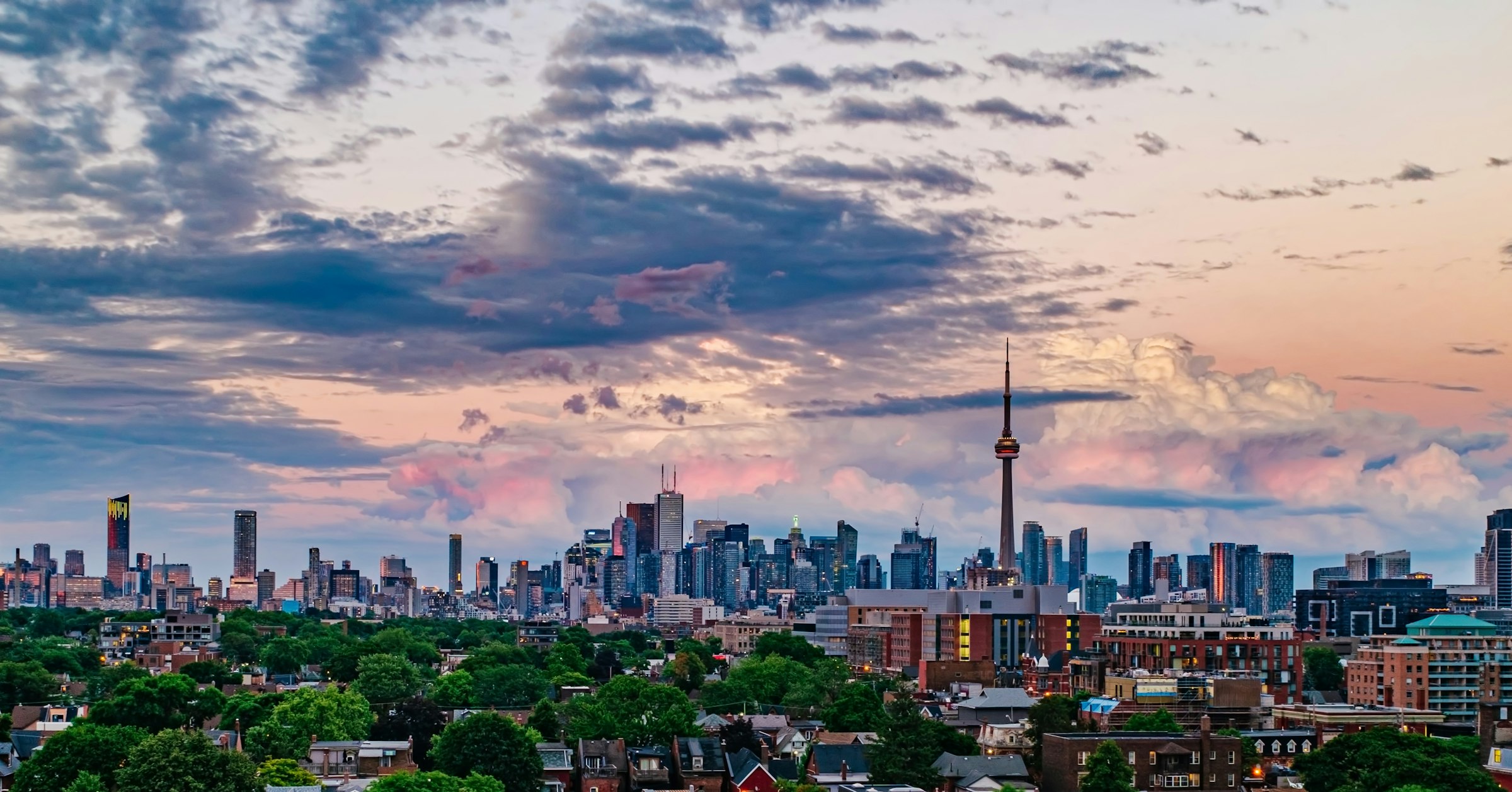 The Toronto downtown skyline under a dramatic dusk sky, the CN Tower rising on the right over the city